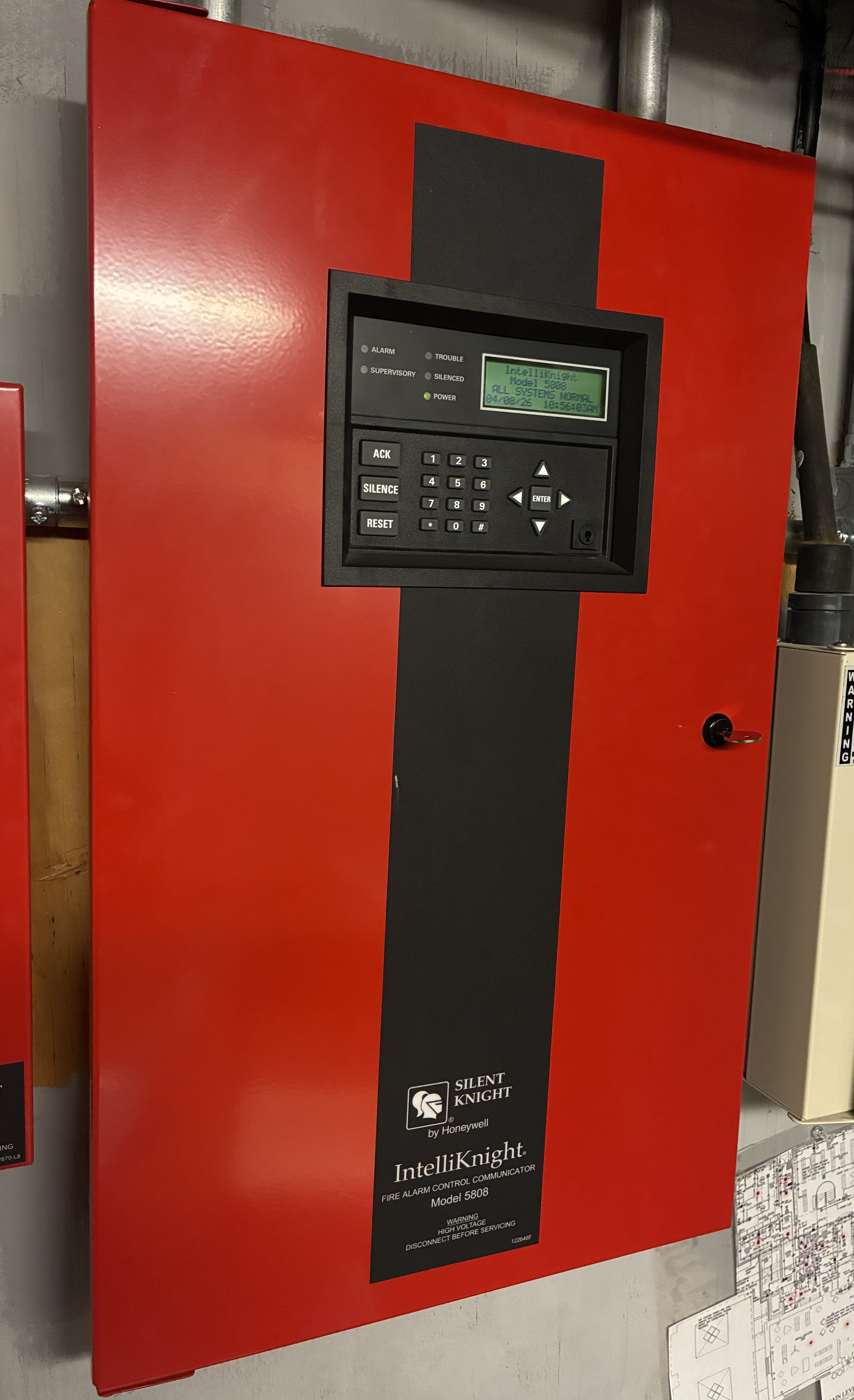 Red Silent Knight fire alarm control panel with a digital display showing all systems normal.